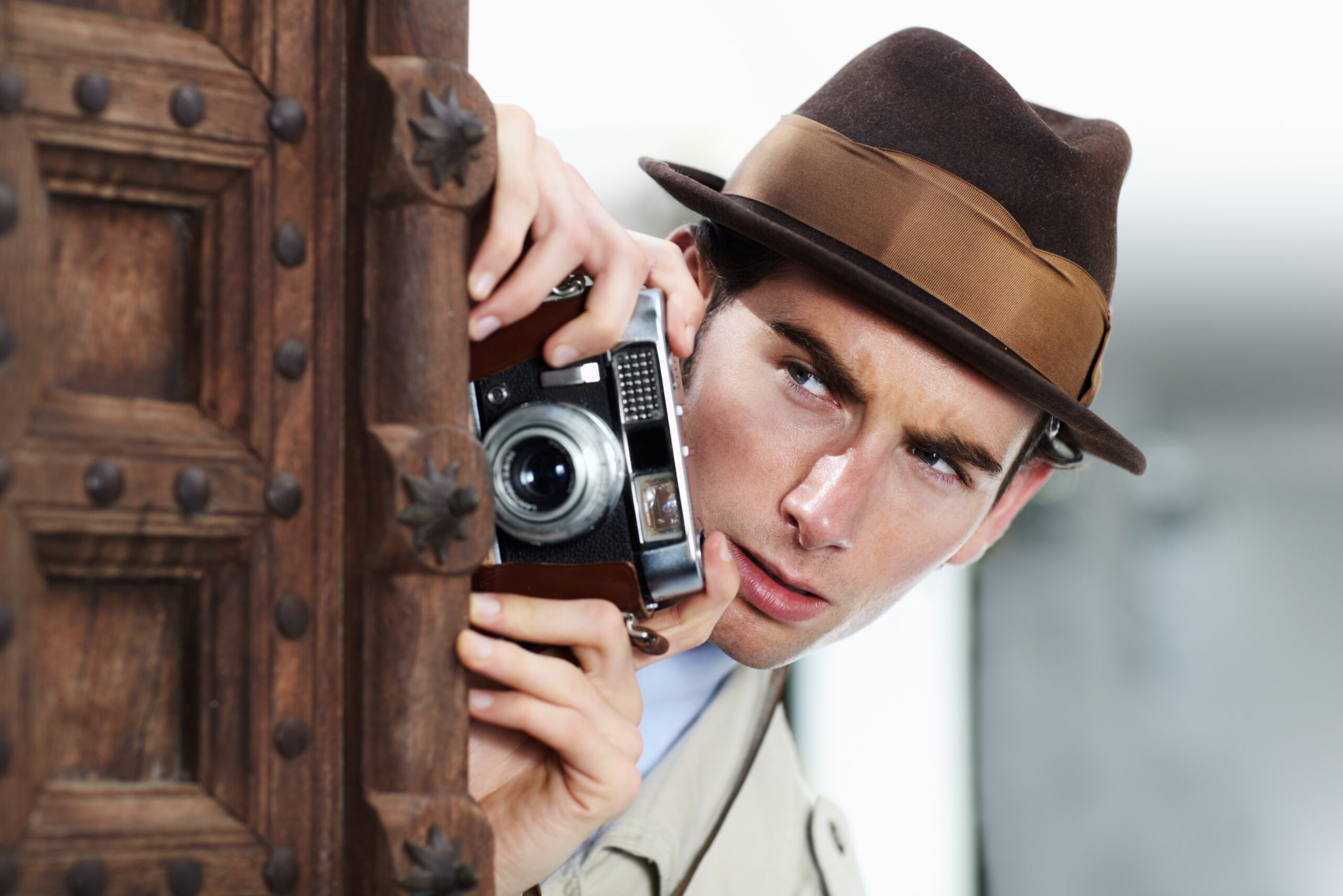 Private detective capturing a photo suspiciously from around a corner while using a retro camera.